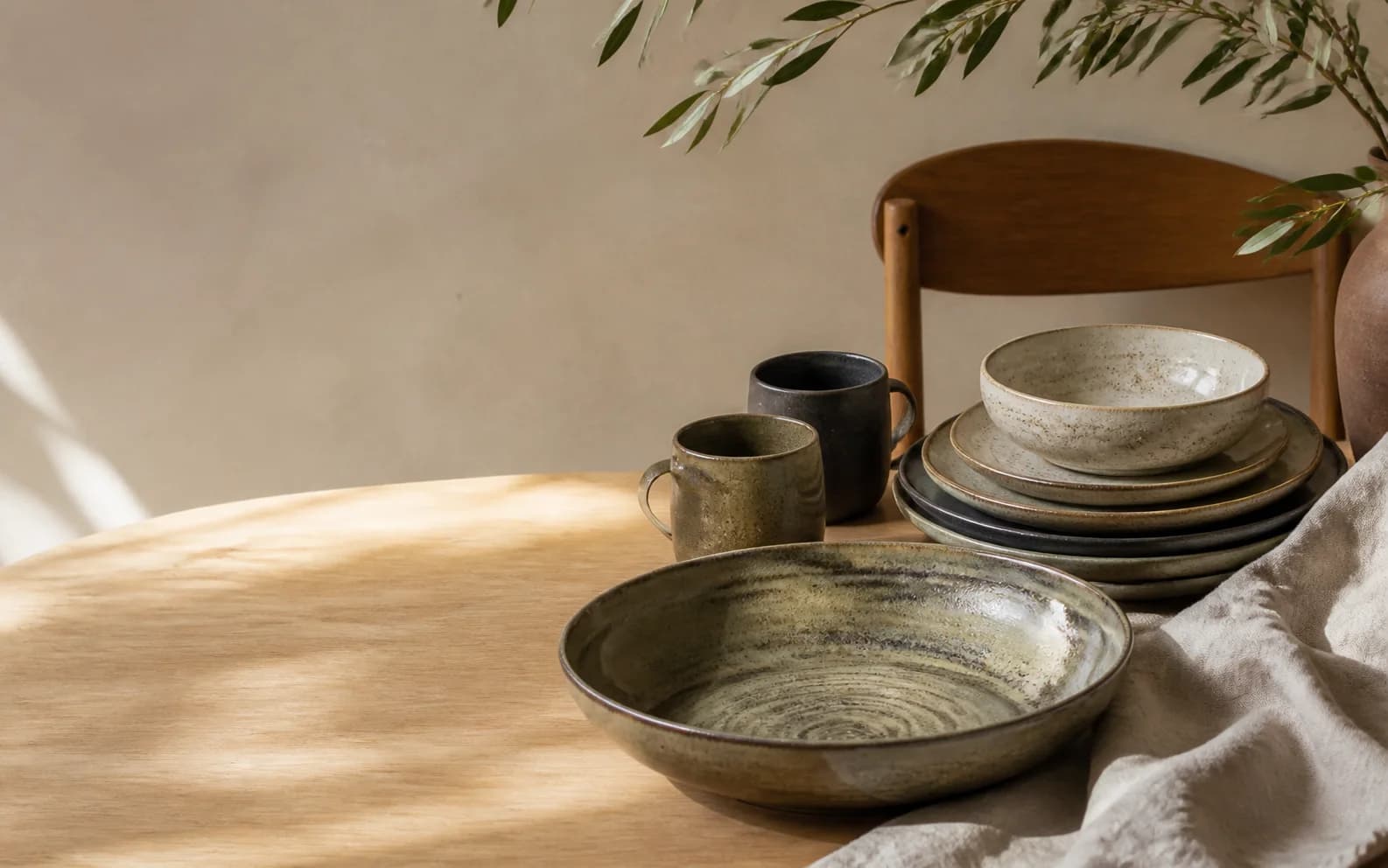 Illustrative stoneware plates, bowls and mugs on a pale oak table